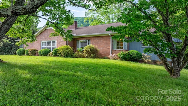 ranch-style home featuring a chimney, a front yard, and brick siding