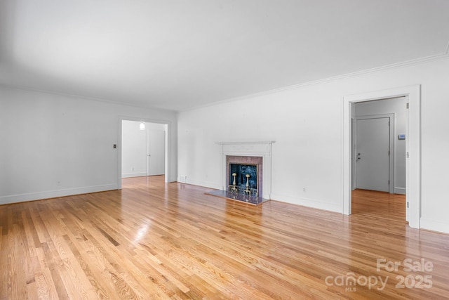 unfurnished living room featuring a high end fireplace, light wood-type flooring, ornamental molding, and baseboards