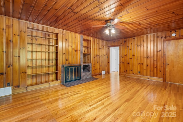 unfurnished living room with wooden walls, light wood-style flooring, ceiling fan, wood ceiling, and built in shelves