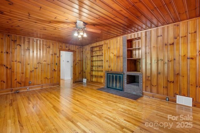 unfurnished living room featuring built in features, wood walls, wood finished floors, ceiling fan, and wood ceiling