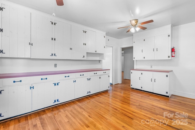 kitchen with ceiling fan, white cabinets, light wood finished floors, baseboards, and light countertops