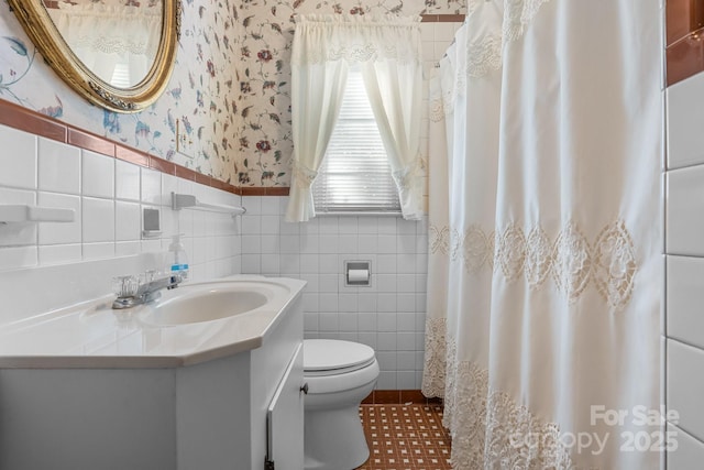 full bath with wallpapered walls, toilet, a wainscoted wall, vanity, and tile walls