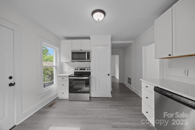 207 Eden St, Davidson, NC 28036 - kitchen with appliances with stainless steel finishes, white cabinetry, light countertops, and light wood finished floors