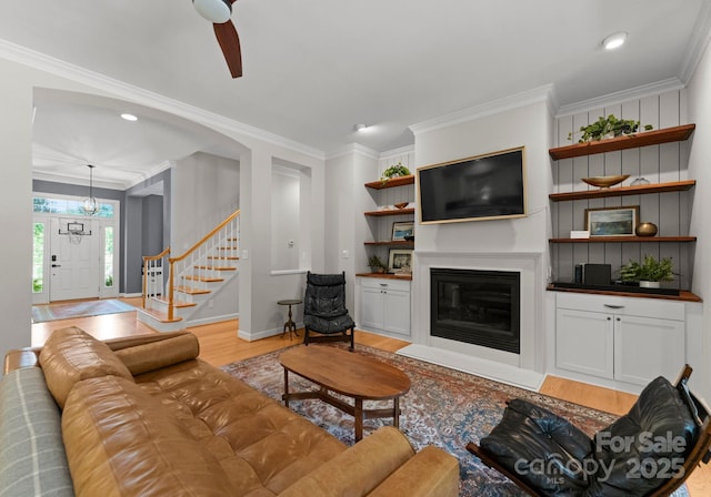 328 Whippoorwill Rd, Mooresville, NC 28117 - living room featuring light wood-style flooring, ornamental molding, a glass covered fireplace, recessed lighting, and stairway