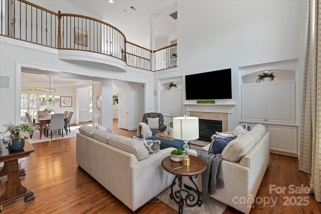 7507 Meadowgate Ln, Waxhaw, NC 28173 - living room with wood finished floors, a glass covered fireplace, a high ceiling, a chandelier, and built in shelves