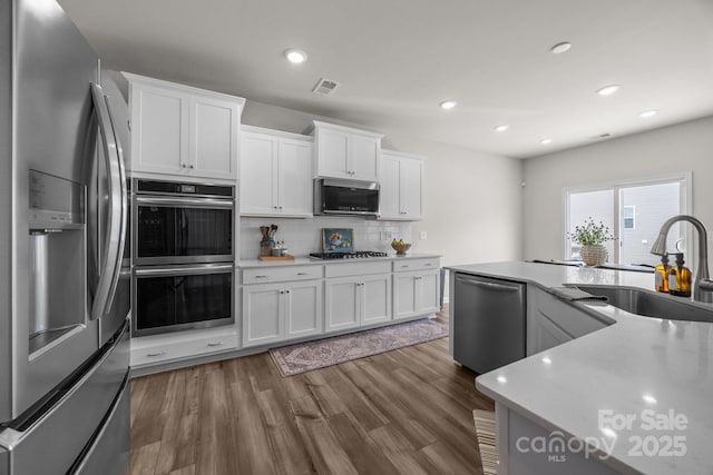 kitchen with appliances with stainless steel finishes, a sink, backsplash, white cabinetry, and recessed lighting