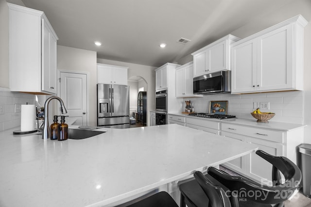 kitchen with appliances with stainless steel finishes, a kitchen bar, decorative backsplash, a peninsula, and white cabinets
