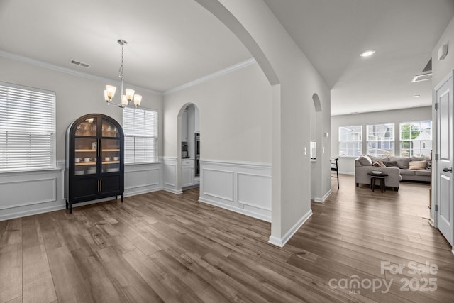 entryway featuring dark wood-style floors, ornamental molding, wainscoting, a chandelier, and arched walkways