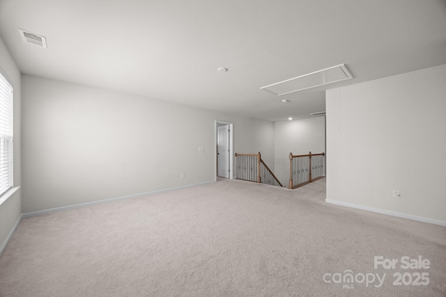 carpeted empty room with attic access and baseboards