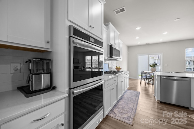 kitchen featuring appliances with stainless steel finishes, decorative backsplash, white cabinetry, and recessed lighting