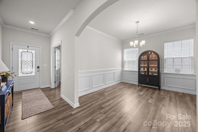 entrance foyer with wood finished floors, arched walkways, a chandelier, ornamental molding, and wainscoting