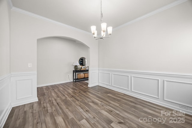 empty room featuring ornamental molding, a chandelier, wainscoting, arched walkways, and dark wood-type flooring