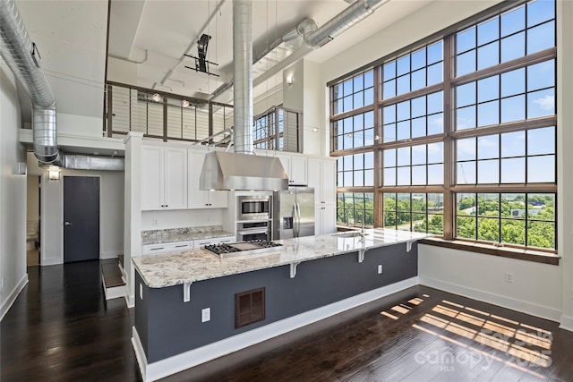 kitchen with appliances with stainless steel finishes, a towering ceiling, baseboards, white cabinets, and dark wood-style flooring