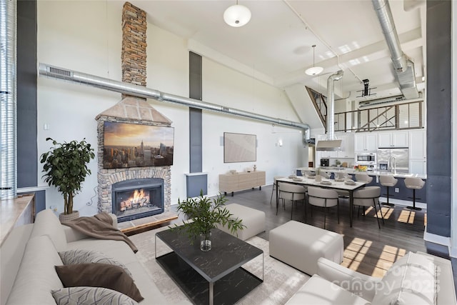 living area with a high ceiling, a stone fireplace, and wood finished floors