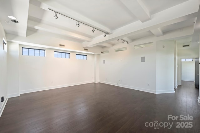spare room featuring rail lighting, beamed ceiling, dark wood-type flooring, and baseboards
