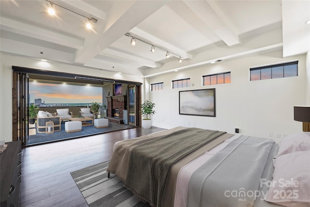 bedroom with rail lighting, beamed ceiling, and wood finished floors