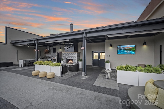 back of house at dusk featuring a patio area, french doors, an outdoor living space with a fireplace, and stucco siding