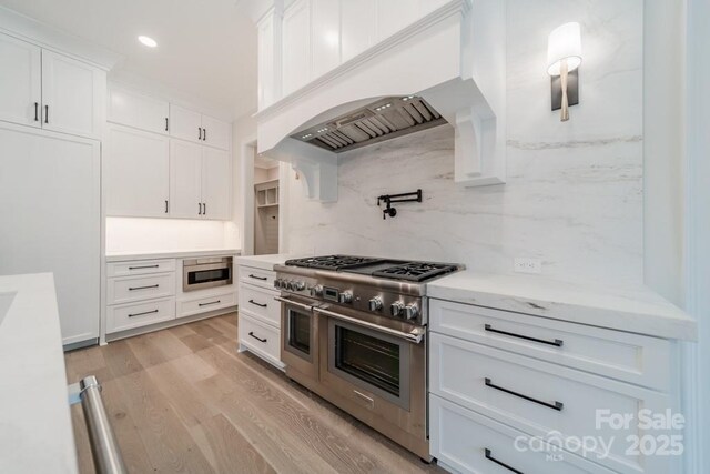 306 Sugar Maple Ln, Weddington, NC 28104 - kitchen with appliances with stainless steel finishes, backsplash, premium range hood, white cabinets, and light wood finished floors