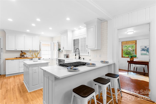 5162 Lincrest Pl, Charlotte, NC 28211 - kitchen featuring white cabinets, crown molding, a breakfast bar area, light countertops, and light wood finished floors