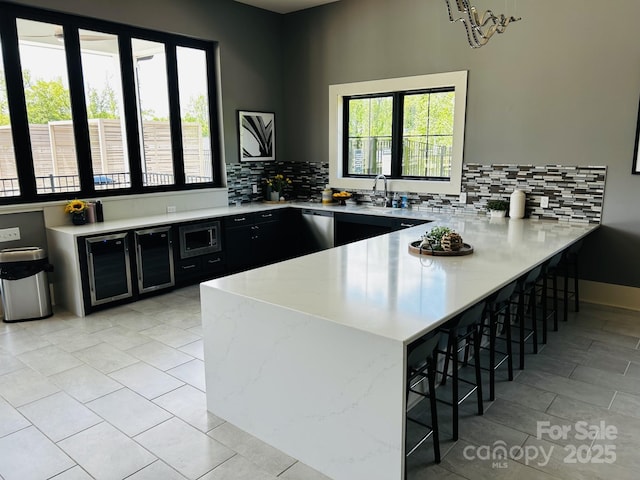 934 Prince Garrett Way, Denver, NC 28037 - kitchen with dark cabinetry, beverage cooler, a peninsula, a breakfast bar, and decorative backsplash
