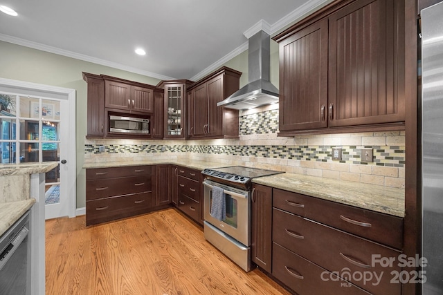 kitchen featuring stainless steel appliances, wall chimney exhaust hood, ornamental molding, light wood-type flooring, and dark brown cabinets