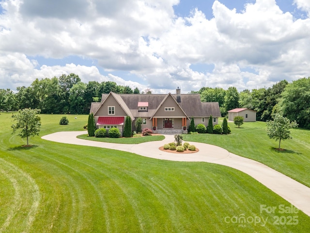 view of front of property featuring curved driveway, a front lawn, a chimney, covered porch, and view of wooded area
