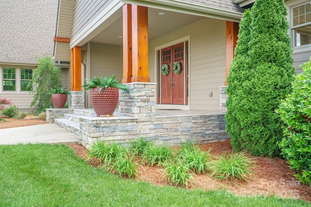 entrance to property featuring stone siding, a porch, and roof with shingles