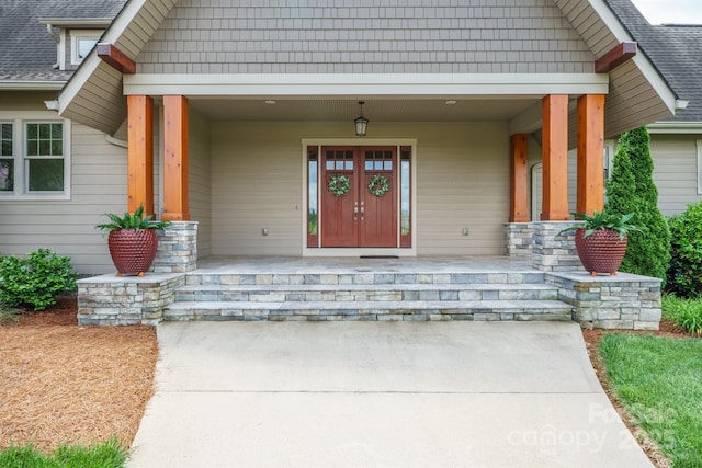 view of exterior entry featuring a porch and a shingled roof