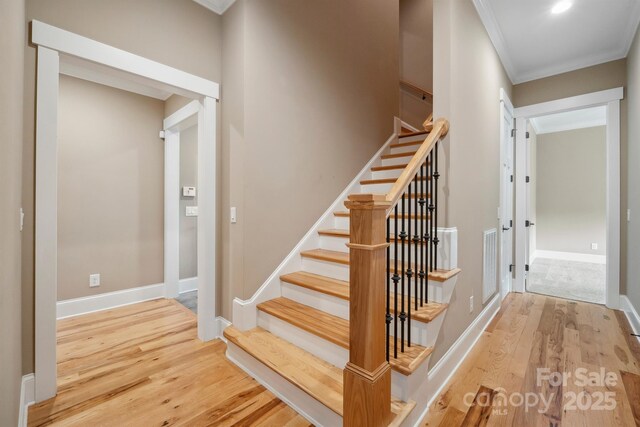 stairway featuring crown molding, wood finished floors, and baseboards