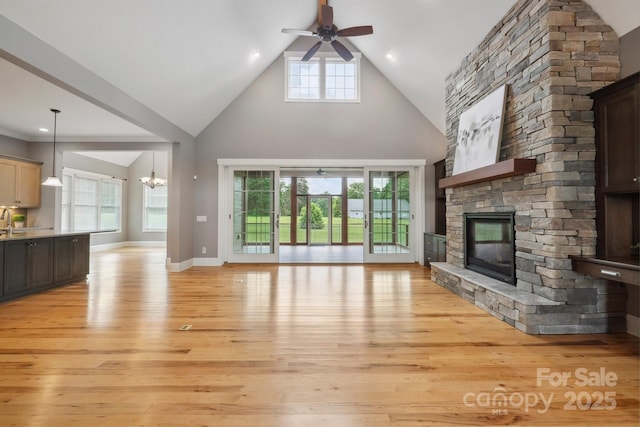 unfurnished living room with a ceiling fan, a stone fireplace, light wood-style floors, high vaulted ceiling, and a chandelier