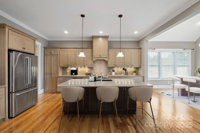 kitchen with high end refrigerator, light wood-type flooring, a sink, light stone counters, and a kitchen breakfast bar