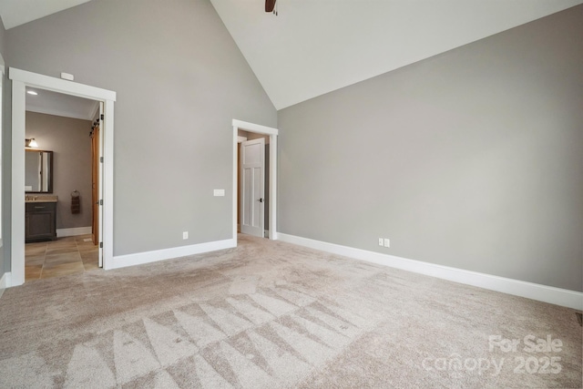 unfurnished bedroom featuring high vaulted ceiling, light carpet, baseboards, and connected bathroom