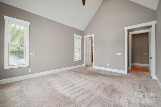 unfurnished bedroom featuring high vaulted ceiling, baseboards, and light colored carpet