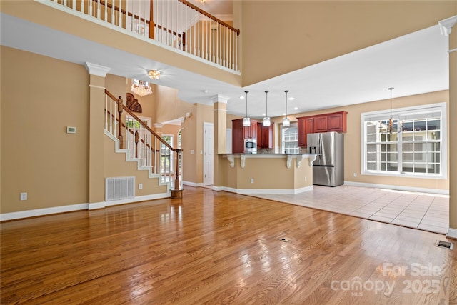 10616 Back Ridge Rd, Charlotte, NC 28277 - unfurnished living room featuring light wood-style floors, ornate columns, baseboards, a high ceiling, and stairs