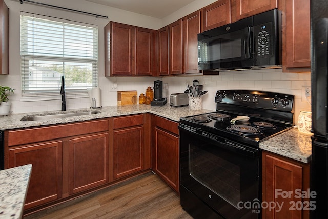 kitchen featuring black appliances, a sink, backsplash, wood finished floors, and light stone counters