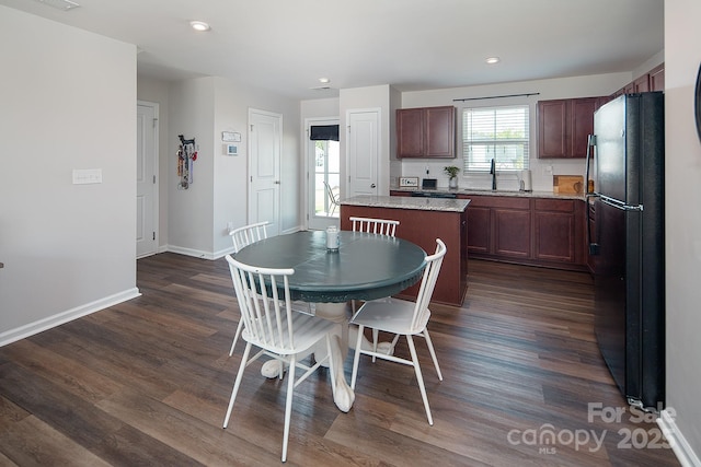 kitchen with freestanding refrigerator, a center island, a sink, dark wood-style flooring, and baseboards