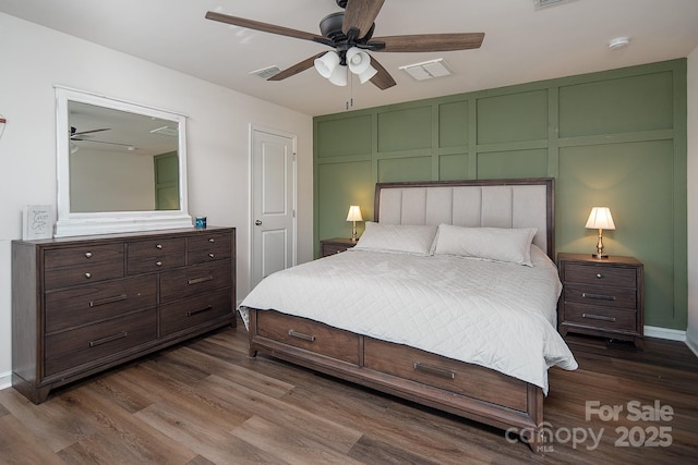 bedroom with dark wood-style flooring, a decorative wall, and a ceiling fan