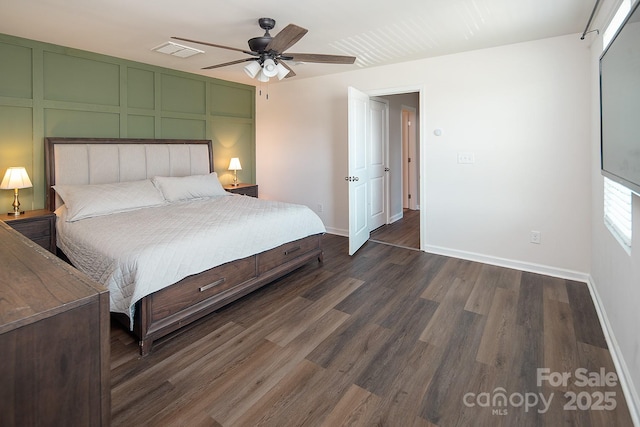 bedroom with dark wood-style floors, a decorative wall, baseboards, and a ceiling fan