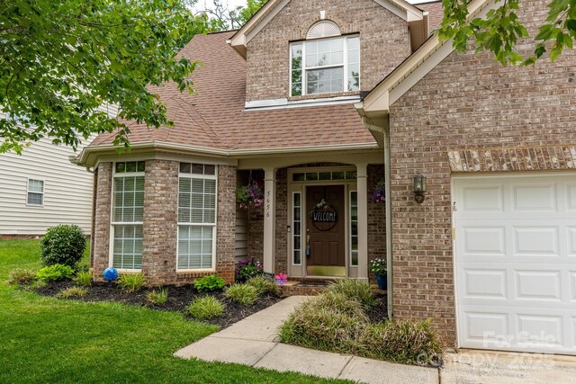 5656 Cambridge Bay Dr, Charlotte, NC 28269 - view of exterior entry featuring brick siding, an attached garage, roof with shingles, and a lawn