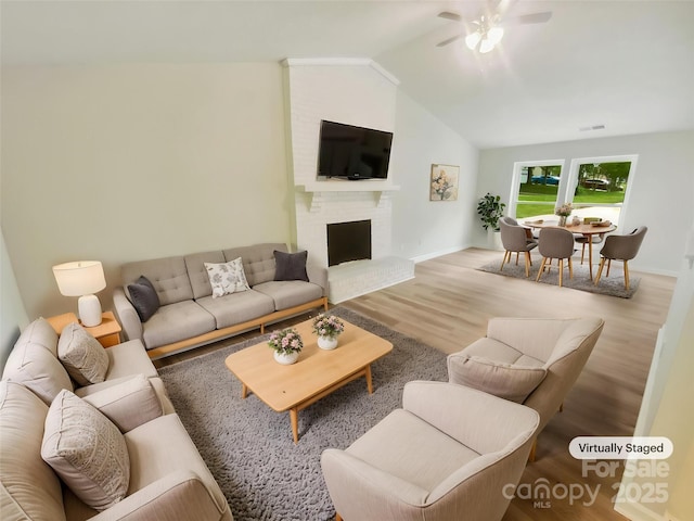living room featuring a ceiling fan, wood finished floors, vaulted ceiling, baseboards, and a brick fireplace