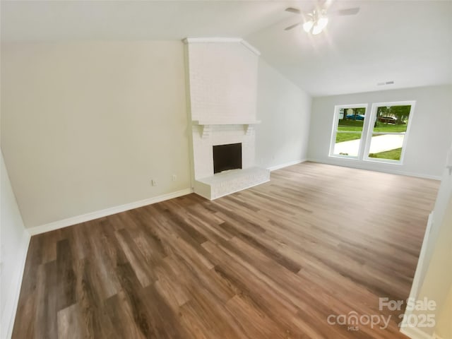 unfurnished living room with ceiling fan, wood finished floors, vaulted ceiling, baseboards, and a brick fireplace
