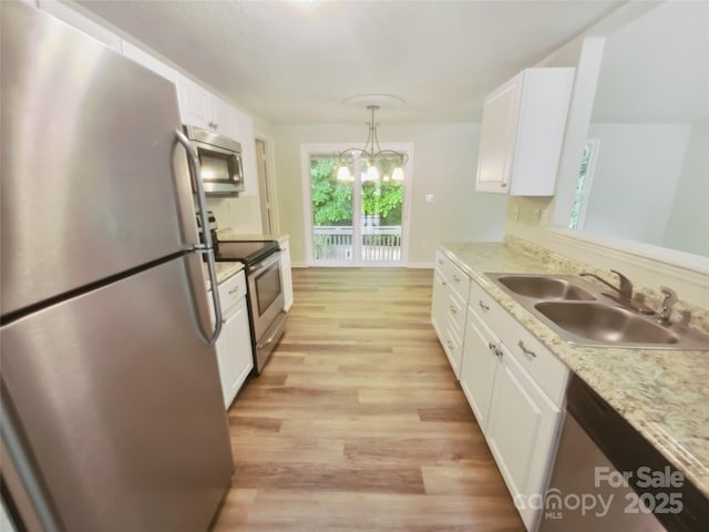 kitchen featuring stainless steel appliances, a sink, white cabinets, light wood finished floors, and pendant lighting