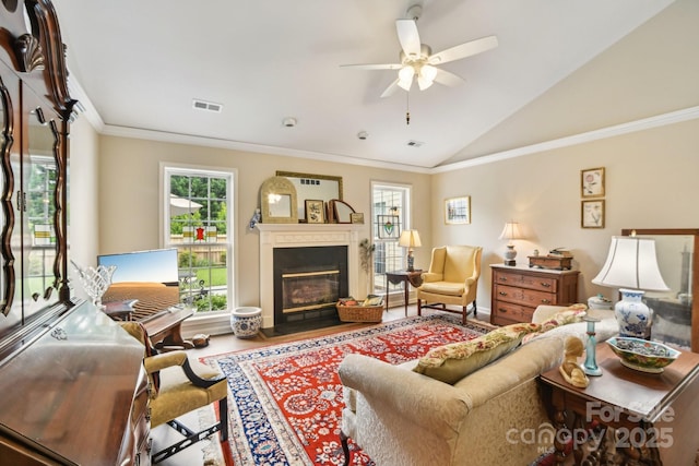 living room with vaulted ceiling, a ceiling fan, a glass covered fireplace, ornamental molding, and wood finished floors