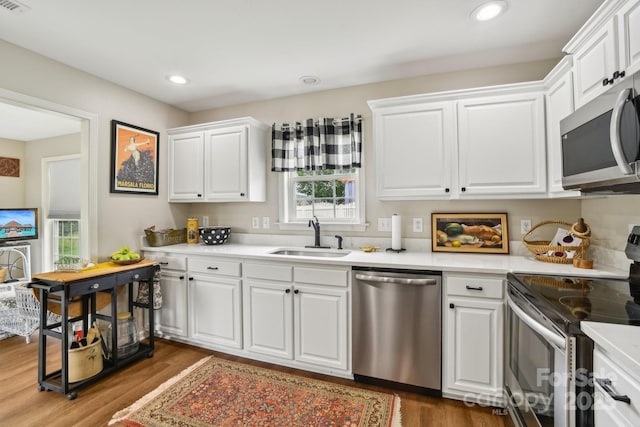 kitchen with stainless steel appliances, a sink, wood finished floors, white cabinets, and light countertops