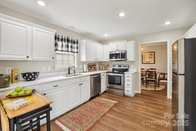 kitchen featuring stainless steel appliances, a sink, white cabinetry, light countertops, and recessed lighting