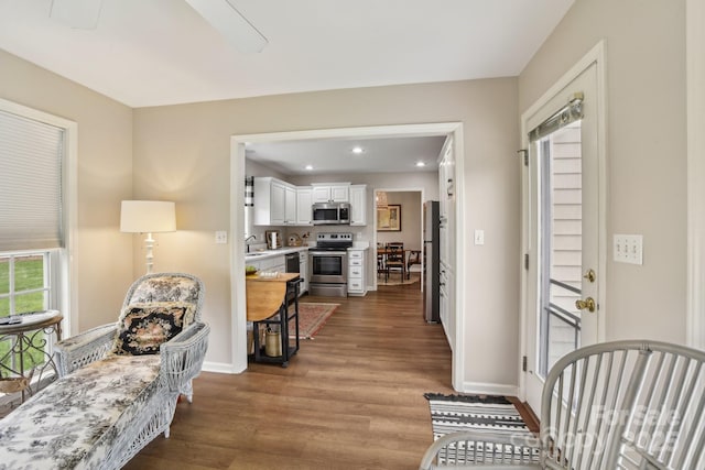 corridor featuring wood finished floors, a sink, baseboards, and recessed lighting