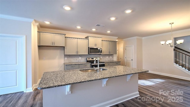 kitchen featuring stainless steel appliances, a sink, gray cabinets, a kitchen breakfast bar, and dark wood finished floors