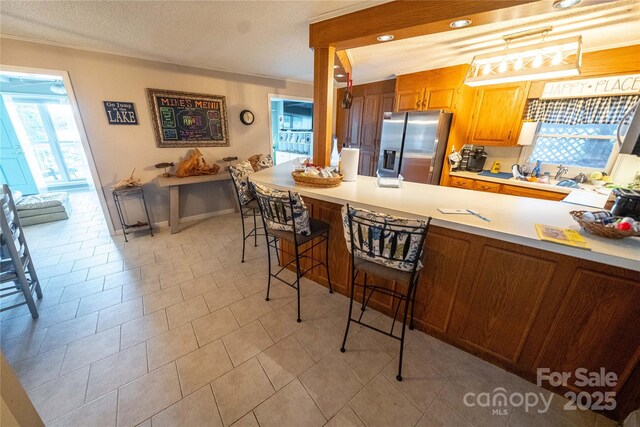 24264 Strand Dr, Albemarle, NC 28001 - kitchen featuring stainless steel refrigerator with ice dispenser, a peninsula, a breakfast bar area, crown molding, and light countertops
