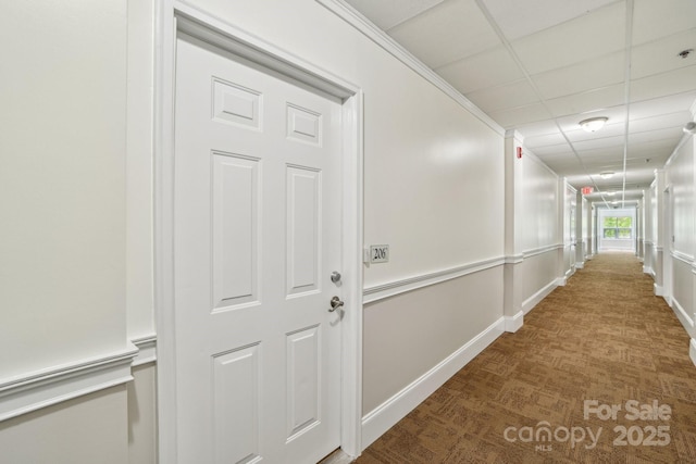 hallway featuring carpet floors, a paneled ceiling, and baseboards