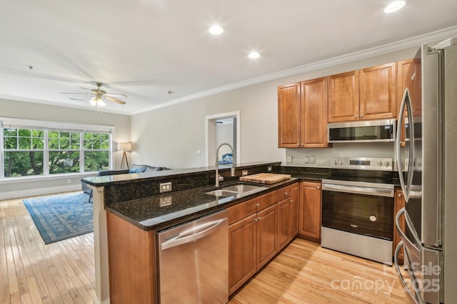 kitchen with stainless steel appliances, a sink, a peninsula, light wood-type flooring, and dark stone counters